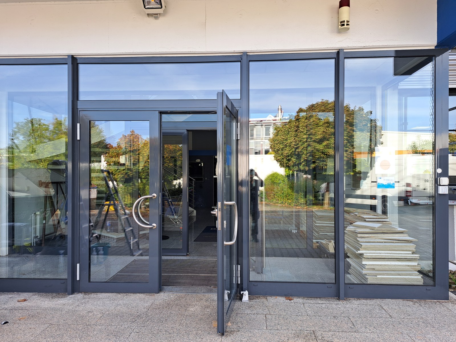 Glasfront mit grauen Rahmen und geöffneter Eingangstür